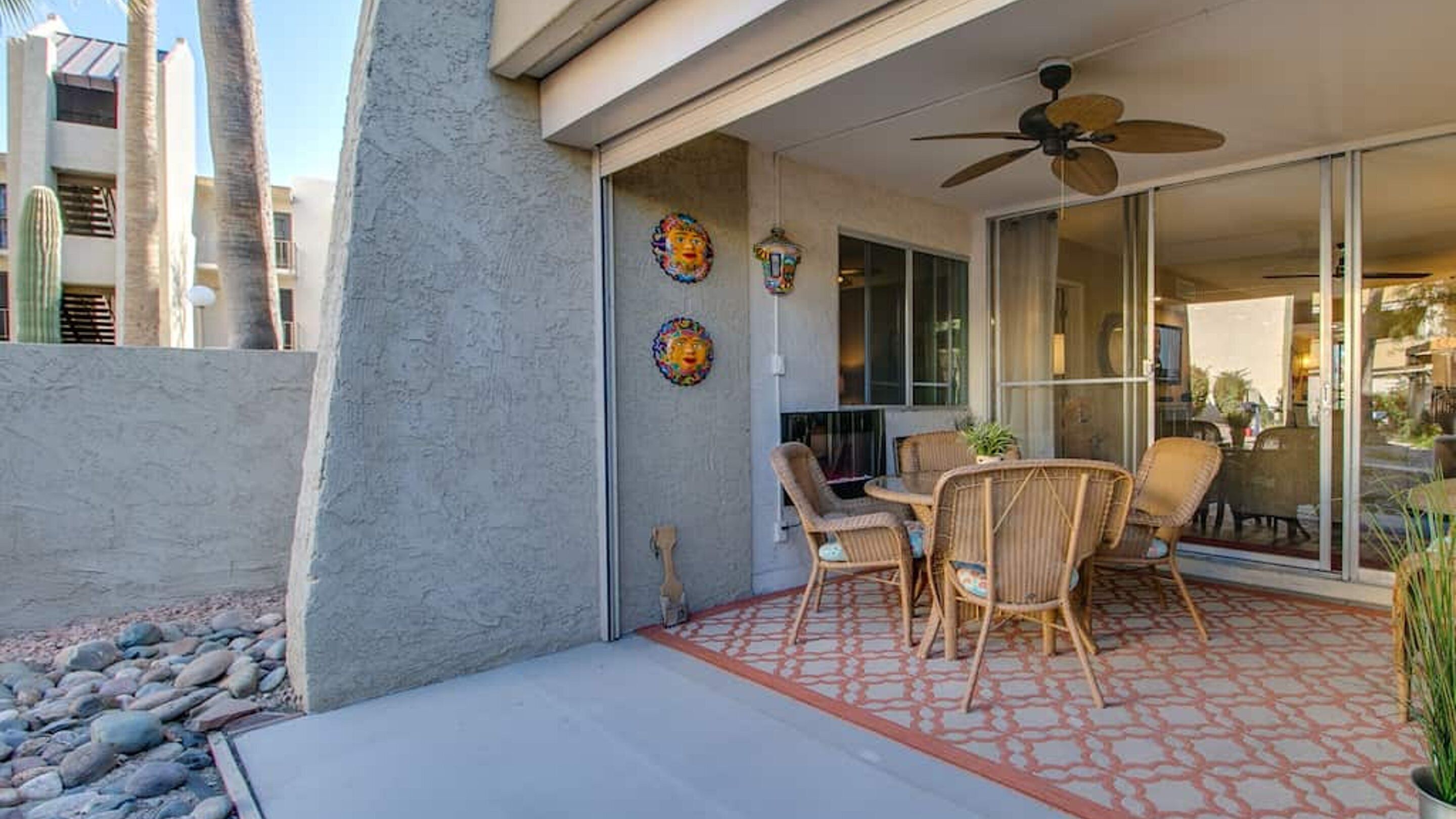 Un patio couvert avec des meubles d’extérieur, un ventilateur de plafond et des éléments décoratifs muraux.