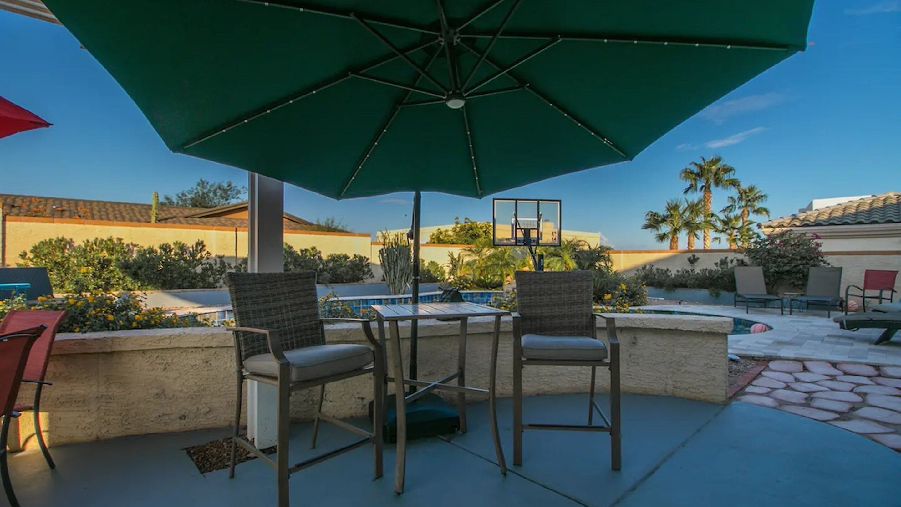 An outdoor patio with a pool, chairs, and a green umbrella.
