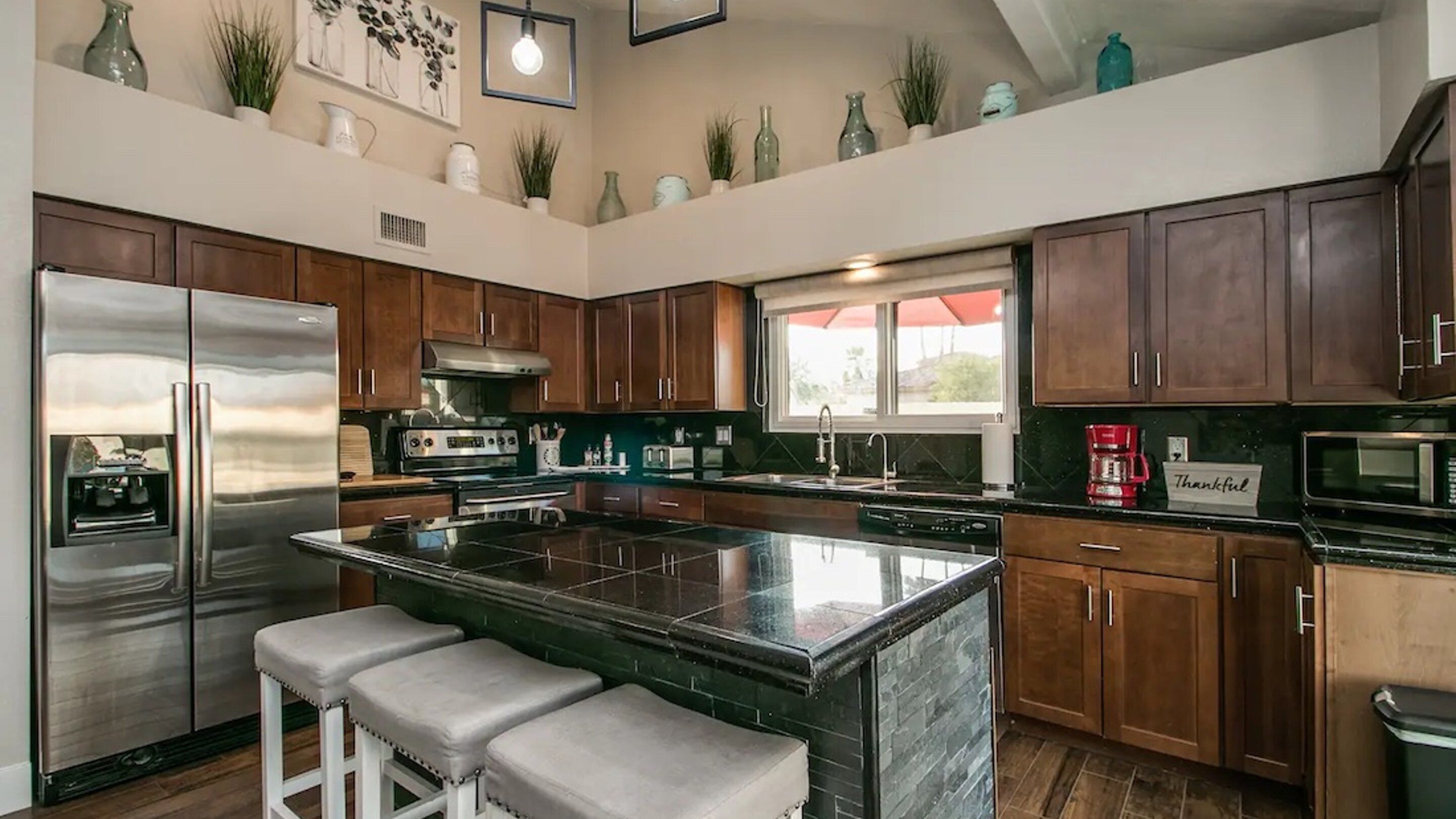 A modern kitchen with a central island, stainless steel appliances, wooden cabinets, and a window with a view.