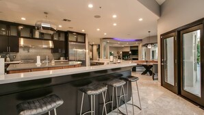 A modern kitchen with a central island, bar stools, and a dining area with a glass door leading outside. - Stunning Private & Modern N. Scottsdale Estate! (Scottsdale)