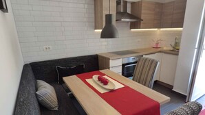 Une cuisine moderne avec des murs en briques blanches, une table à manger en bois agrémentée d’un chemin de table rouge et un luminaire suspendu noir.