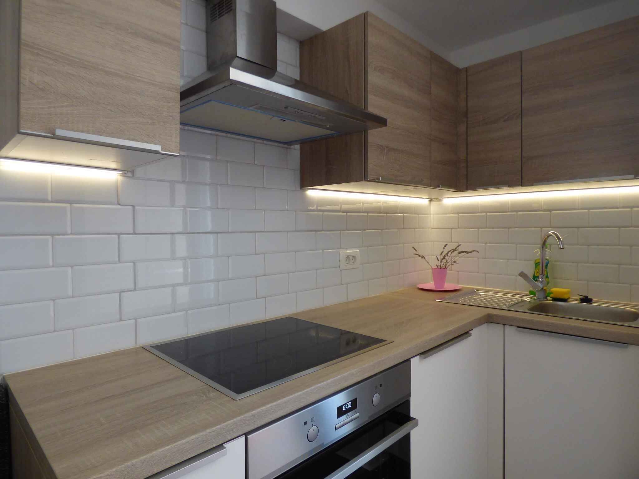 A modern kitchen with white subway tiles, wooden cabinets, a stainless steel range hood, and a built-in oven.