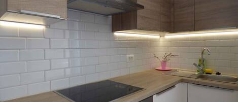 A modern kitchen with white subway tiles, wooden cabinets, a stainless steel range hood, and a built-in oven.