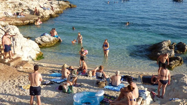 Une plage où l’on voit des gens se prélasser au soleil, nager et des bateaux sur l’eau.