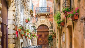 Un estrecho callejón con edificios de piedra, una puerta de madera y mesas y sillas dispuestas para comer.