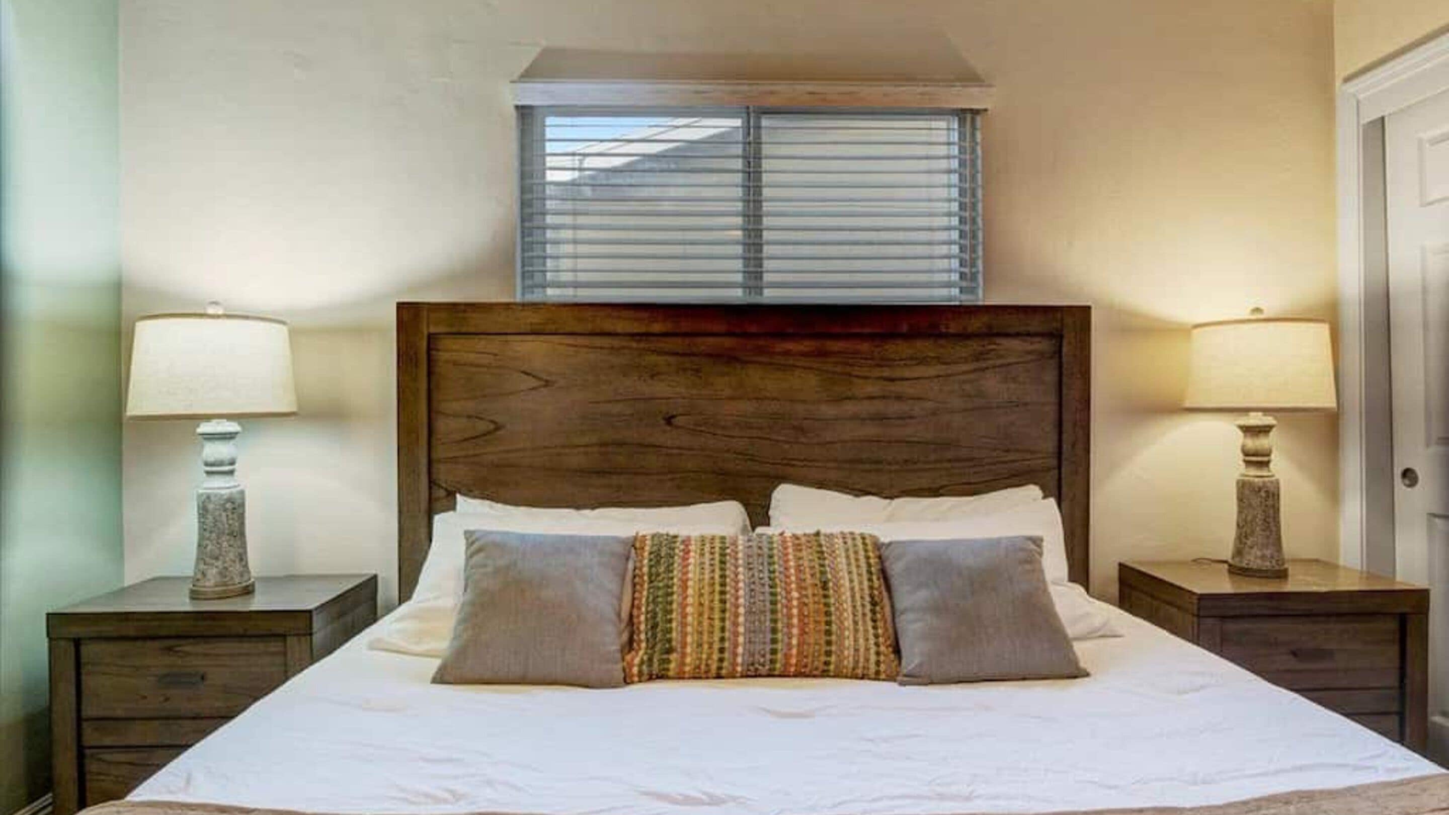 A neatly made bed with a wooden headboard, two bedside lamps, and a window above.