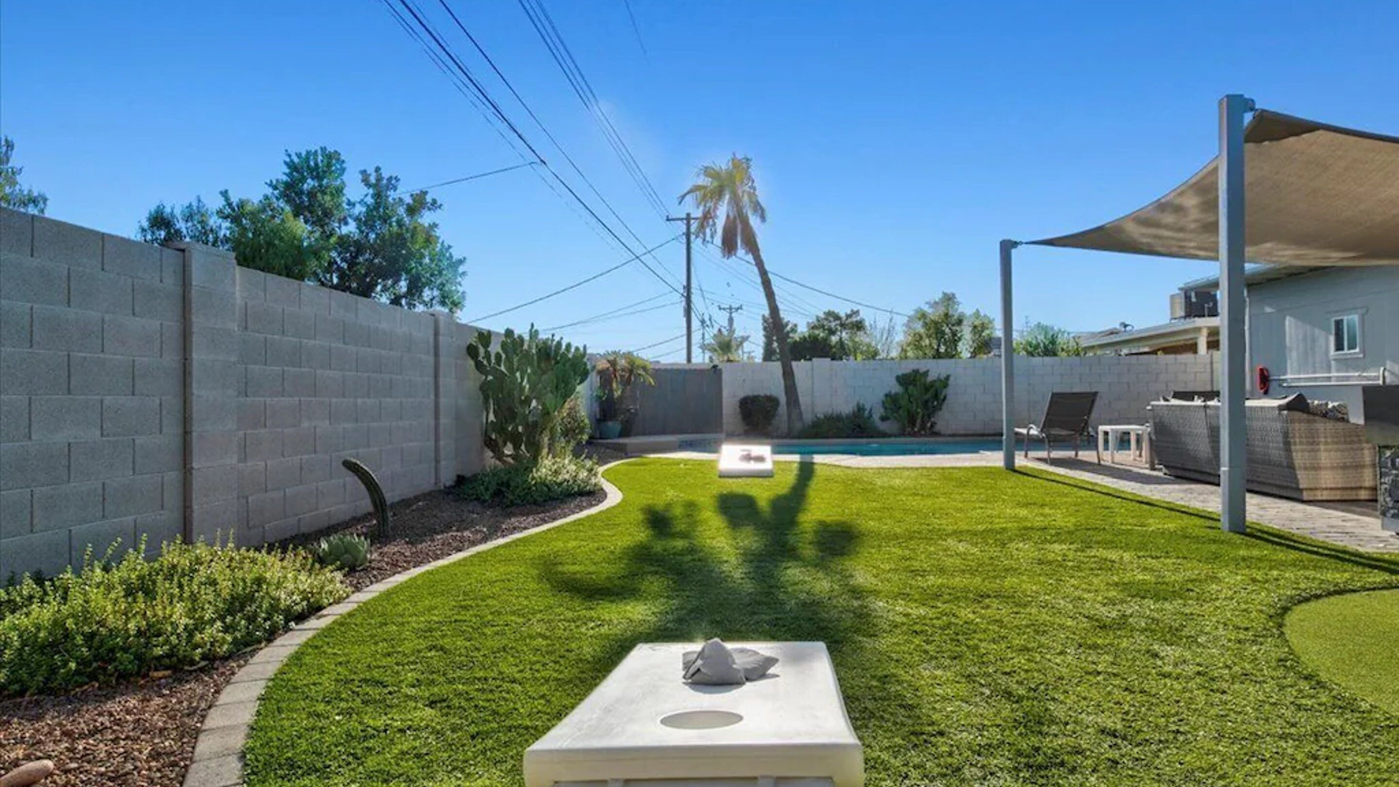 A backyard with a pool, a covered seating area, and a well-maintained lawn.