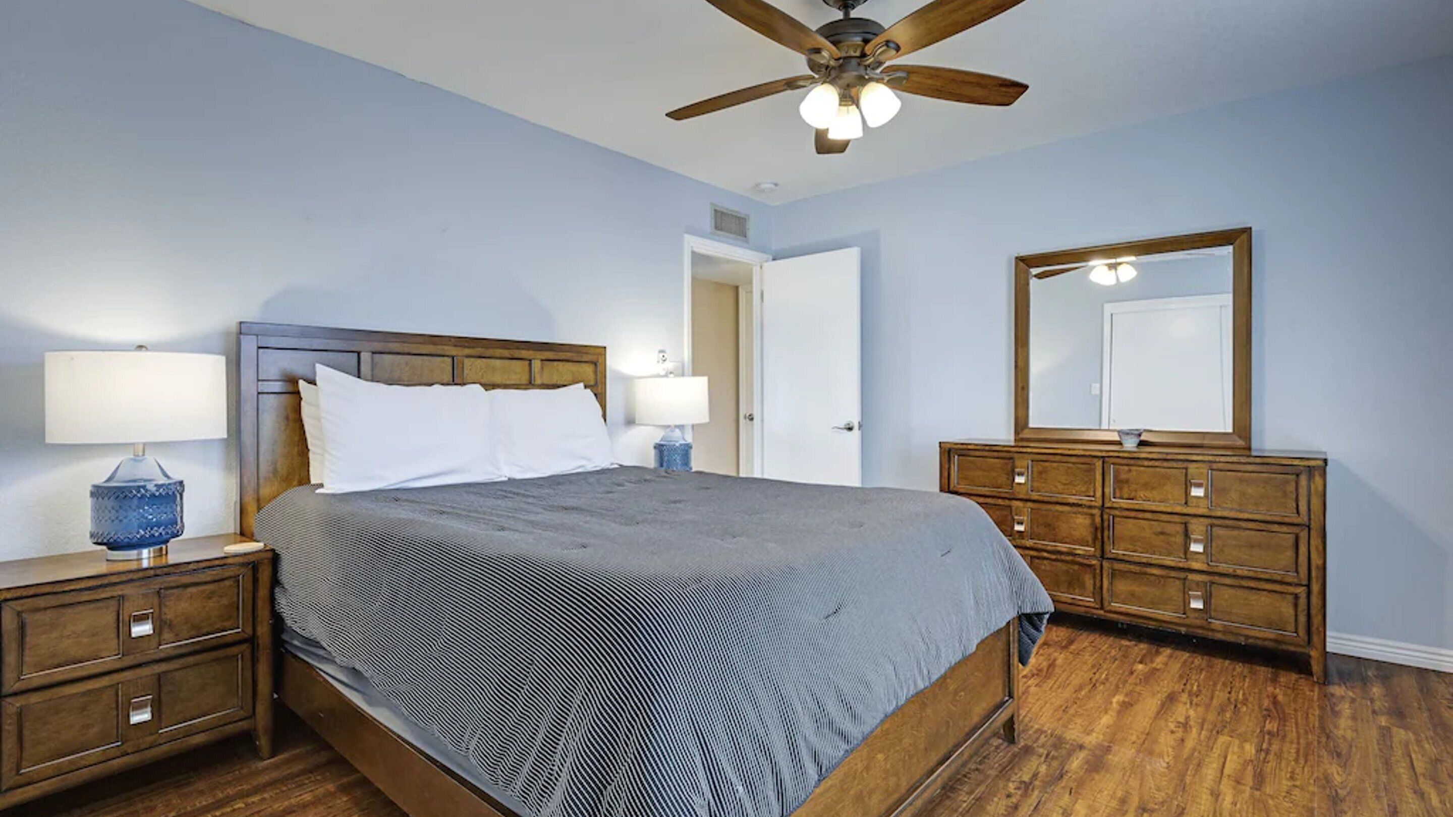 A bedroom with a bed, nightstands, a dresser, a ceiling fan, and a mirror.