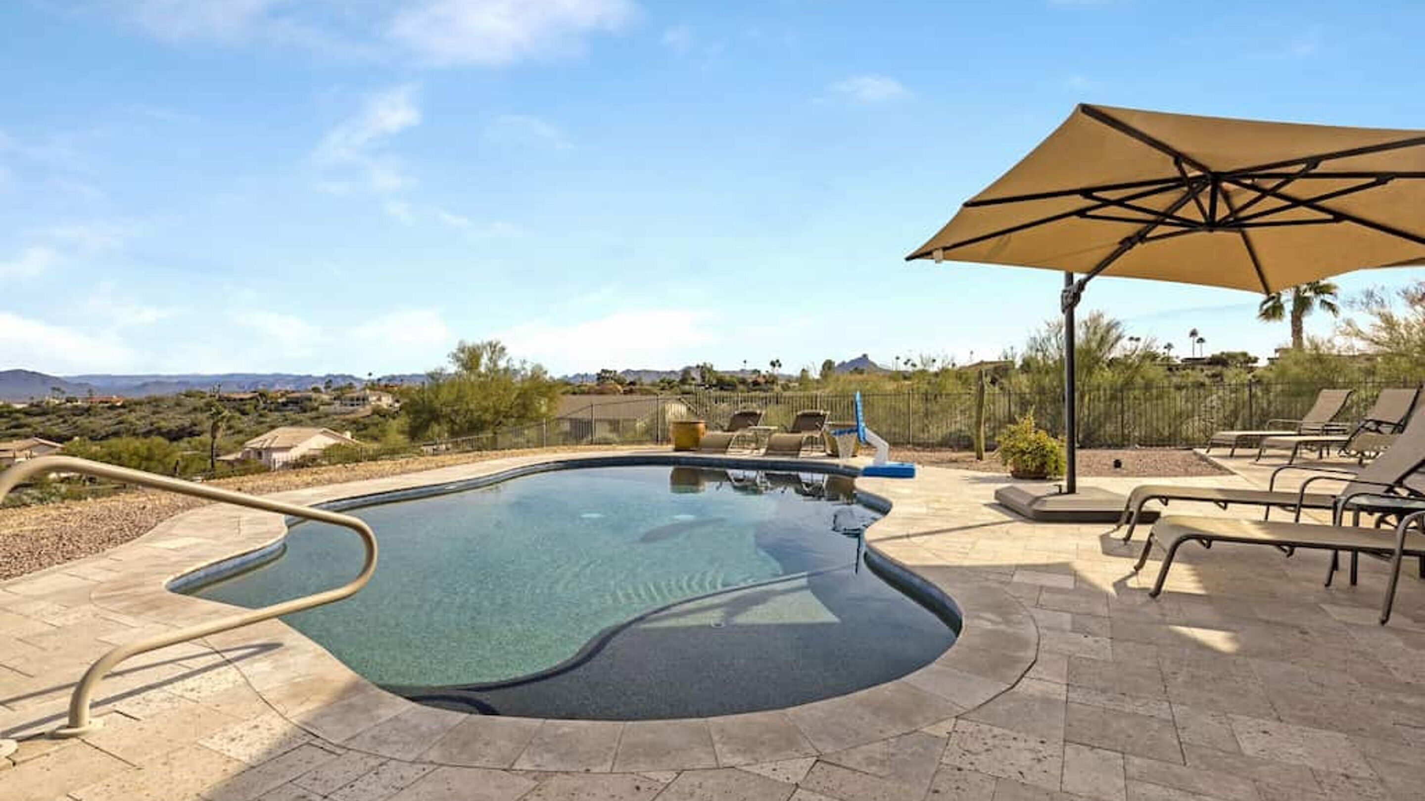 A swimming pool with a hot tub, lounge chairs, and a large umbrella.
