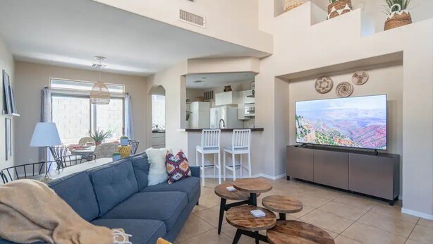 A modern living room with a sofa, a TV, and a dining area with chairs and a table.
