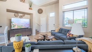 A modern living room with a large flat-screen TV, grey sofas, a coffee table, and a lamp.