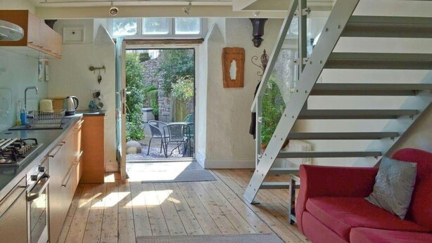 A modern kitchen with a dining area, a red sofa, and a staircase leading to a balcony. - Church Conversion 3-bed House in Centre of Kendal (Kendal)