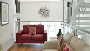 A modern living room with a red sofa and a beige sofa, a patterned rug, a wall art piece, and a statue on a small table. - Church Conversion 3-bed House in Centre of Kendal (Kendal)