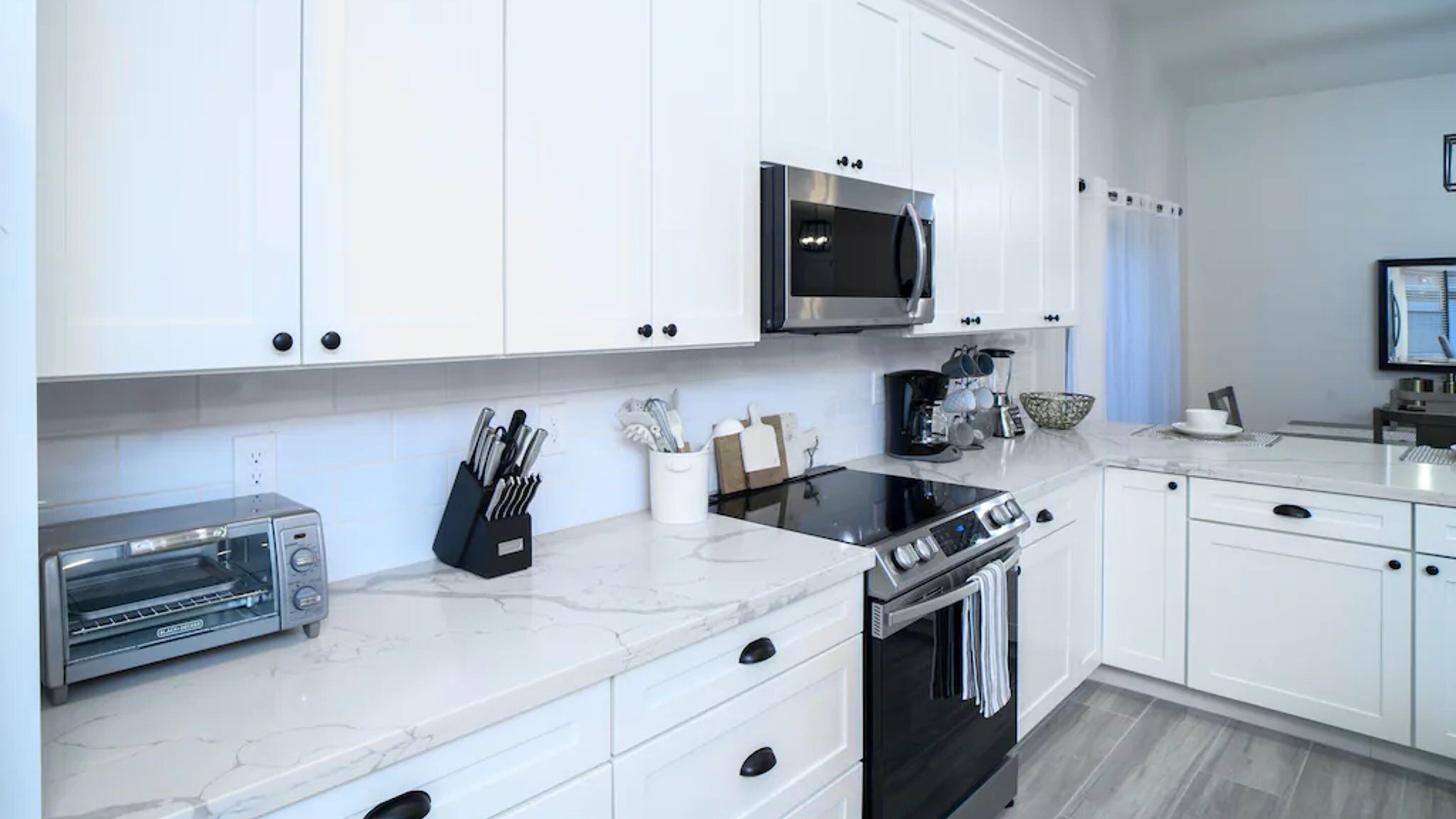 A modern kitchen with white cabinets, a microwave, a toaster, and a stove.