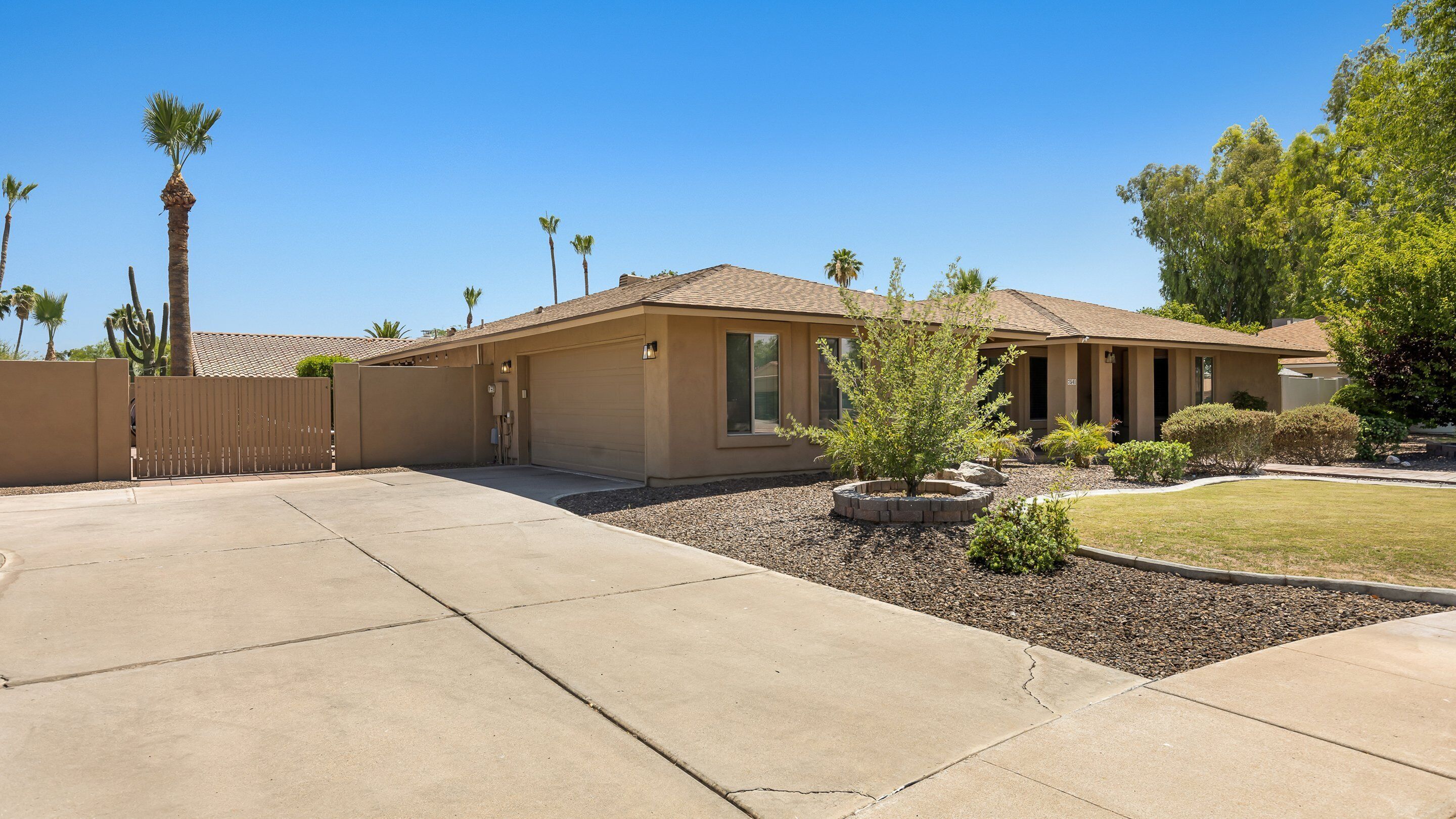 A single-story house with a beige exterior, a tiled roof, and a front yard with a small tree and shrubs.