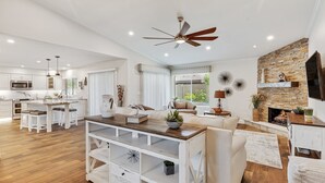 Een ruime woonkamer met een keuken, een eettafel en een open haard.