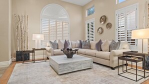 A living room with a beige sofa, patterned cushions, a marble coffee table, and decorative wall art. - Massive North Scottsdale 6 Bdrm w/ Oasis Backyard! (Scottsdale)