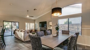 Un salon spacieux avec une grande table à manger, des chaises à motifs, une cheminée et un ventilateur de plafond.