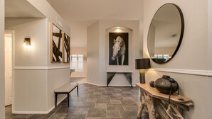 Un couloir avec un banc, un miroir fixé au mur et un tableau encadré.
