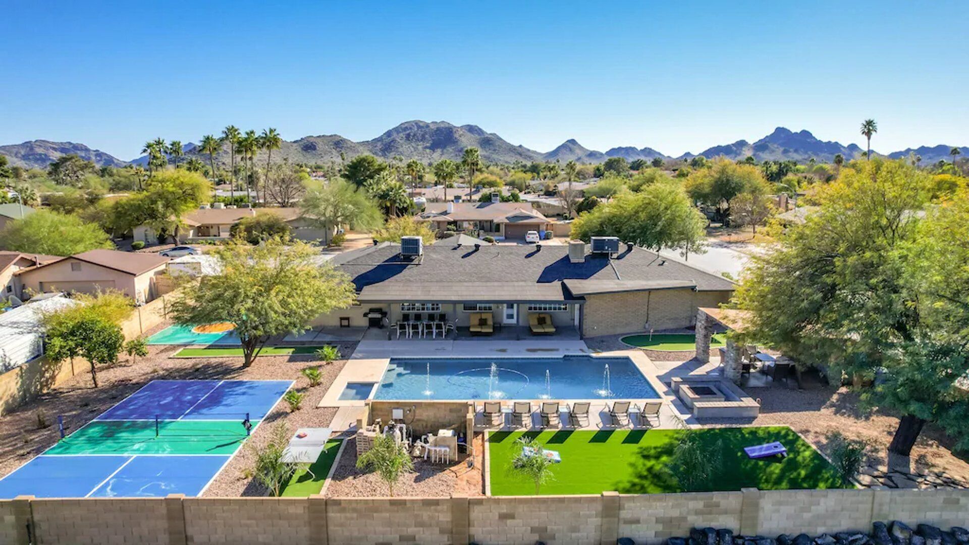 A residential property with a swimming pool, tennis courts, and a mountain backdrop.