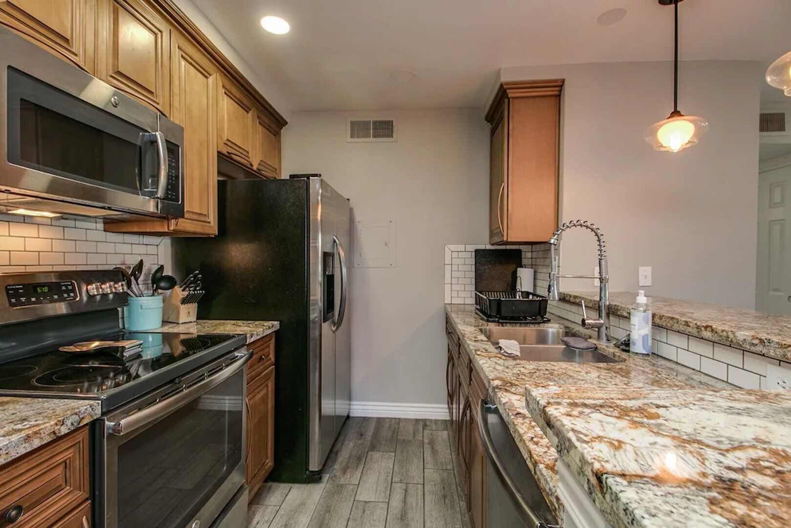 A modern kitchen with stainless steel appliances, wooden cabinets, granite countertops, and pendant lighting.