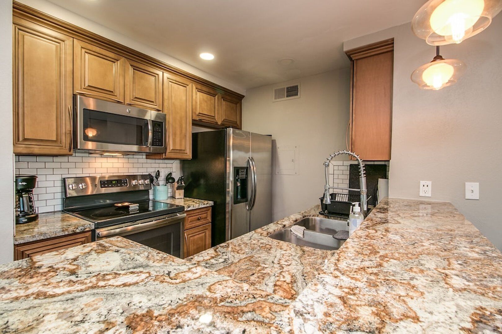 A modern kitchen with granite countertops, stainless steel appliances, wooden cabinets, and a built-in microwave.