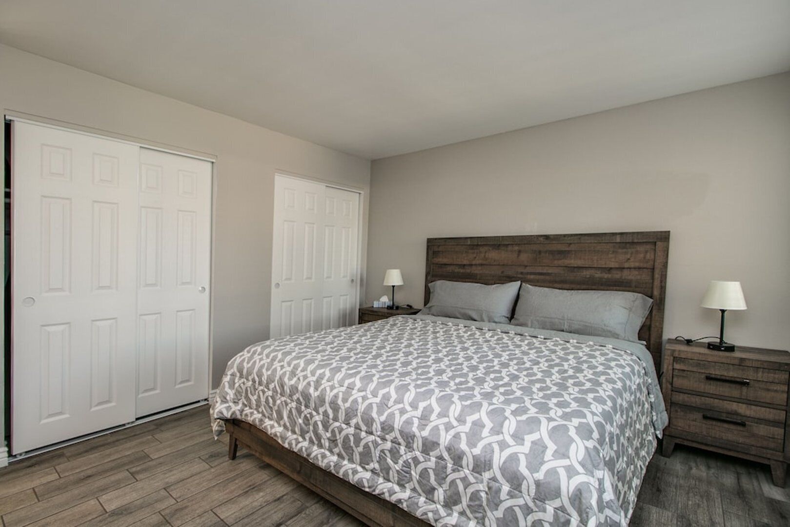 A bedroom with a bed, two nightstands, a wooden headboard, and a white door.