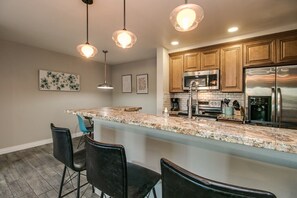 A modern kitchen with granite countertops, stainless steel appliances, and bar seating.