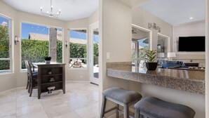 A modern kitchen with a granite countertop, a dining area with a table and chairs, and a large window offering a view of greenery. - Amazing Home in Great Location W/backyard Oasis! (Scottsdale)