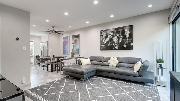 A modern living room with a sectional sofa, a dining area with a glass table, and a large abstract painting on the wall. - Unbeatable Old Town Location! Modern and Classy! (Scottsdale)