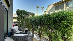 Ein Patio mit Korbmöbeln und einem kleinen Tisch, umgeben von dichtem Grünwerk und Palmen.