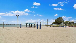 A beach volleyball court with a net, benches, and a covered seating area.