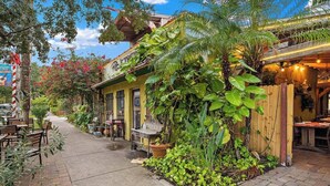 A cozy outdoor seating area with tables and chairs, surrounded by lush greenery and a wooden fence.