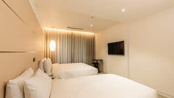 A hotel room with two beds, a small table, a wall-mounted TV, and a ceiling vent.