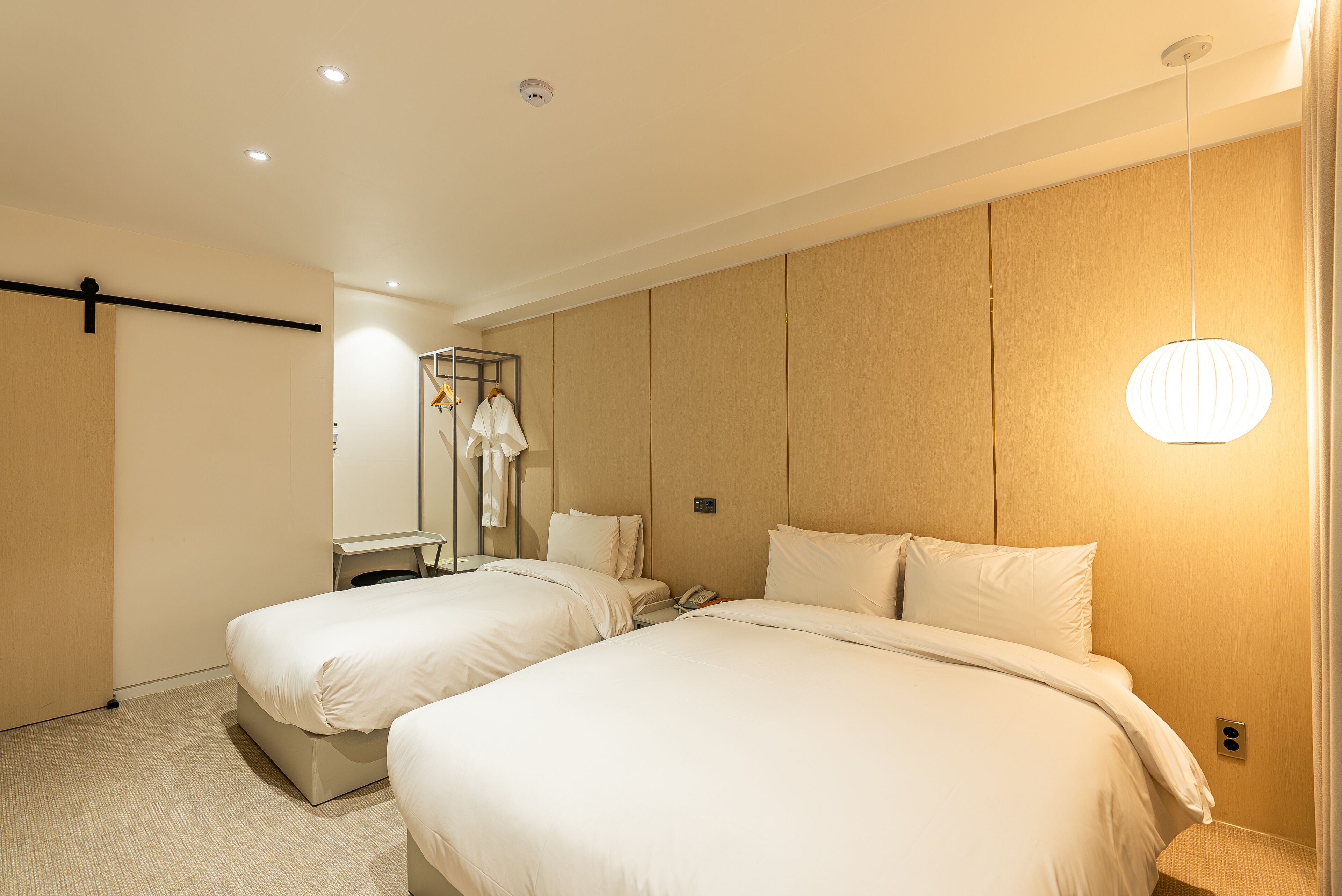 A hotel room with two beds, a mirror, a hanging light fixture, and a coat rack.