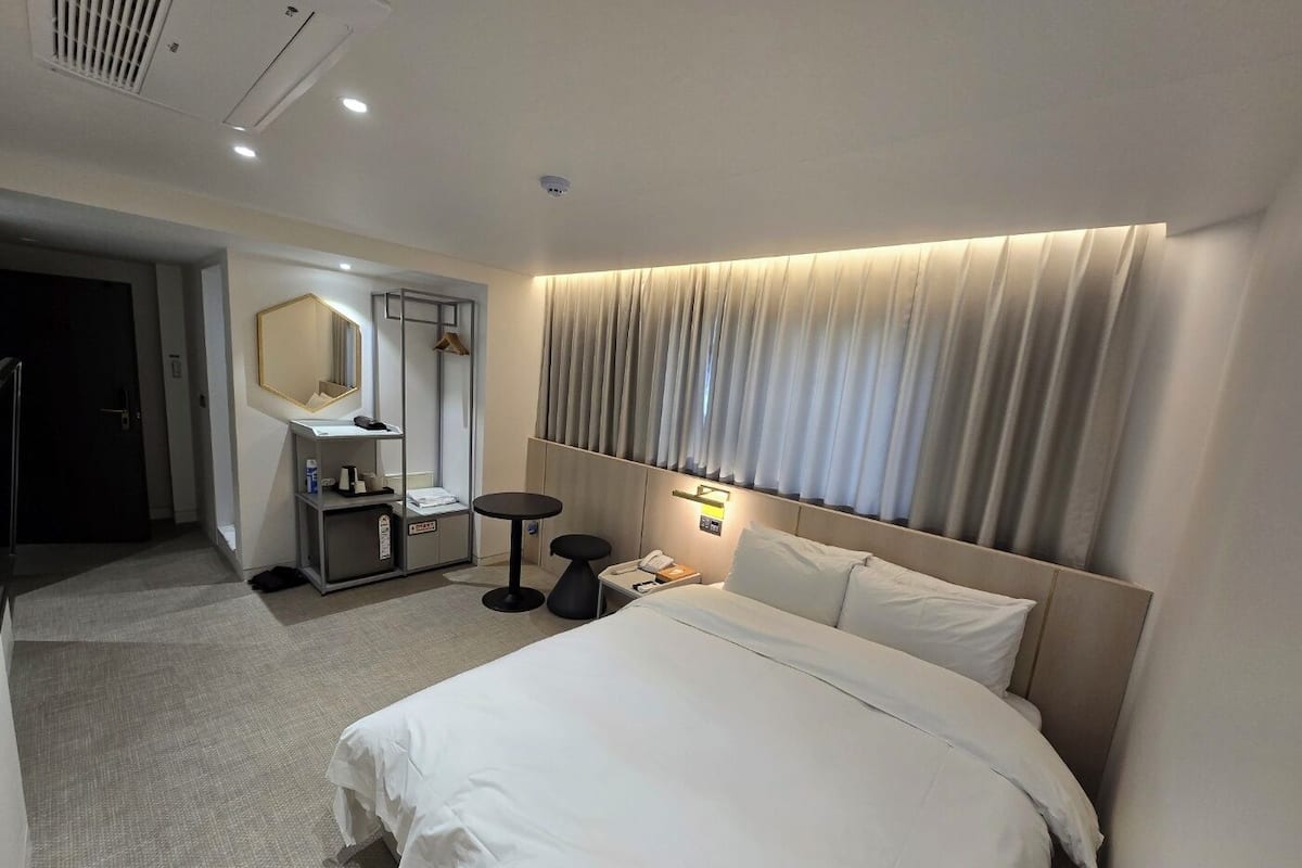 Een hotelkamer met een bed, bureau, spiegel, kledingkast en badkamer.