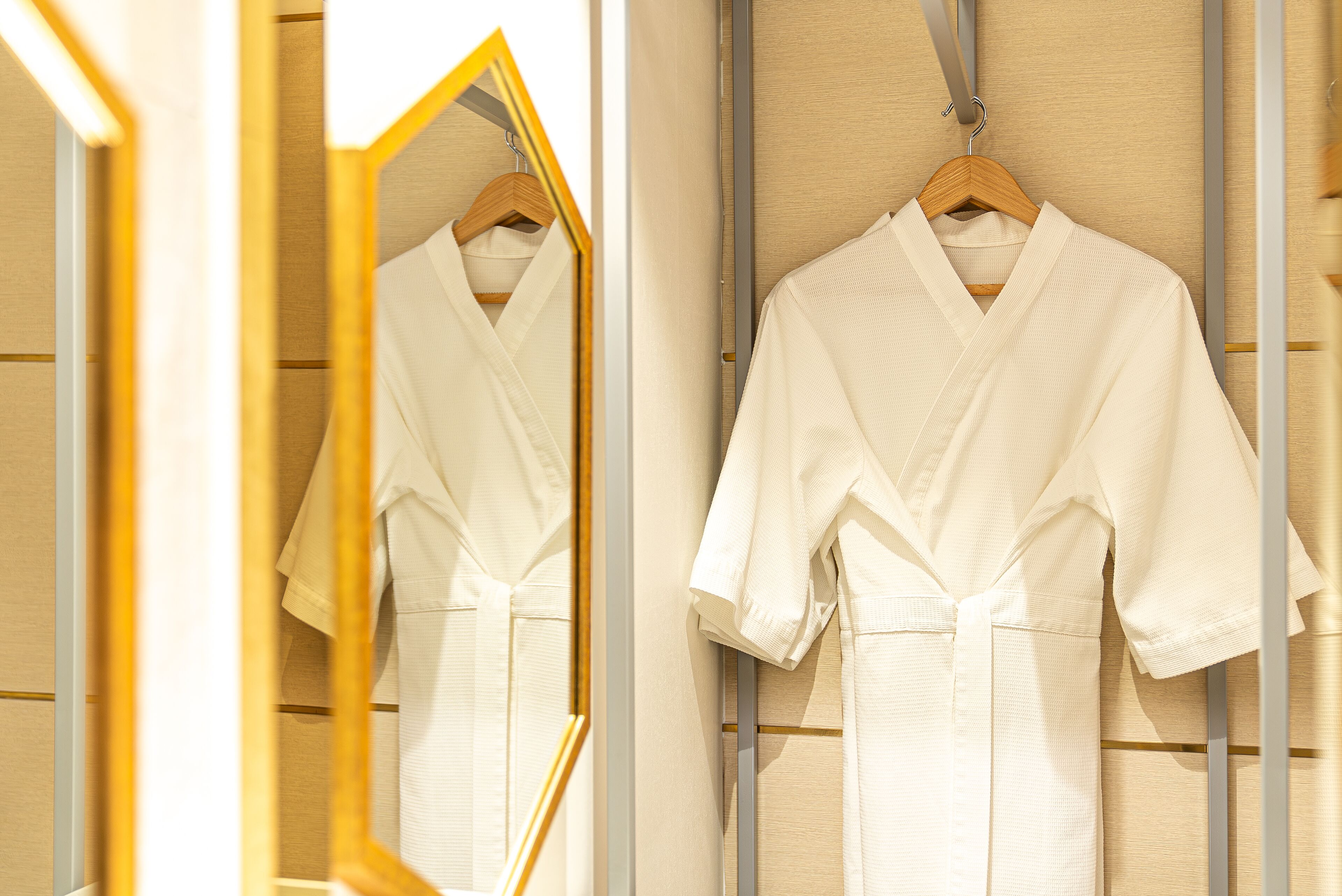A white robe hanging on a wooden hanger in a room with wooden paneling and a mirror reflecting the robe.