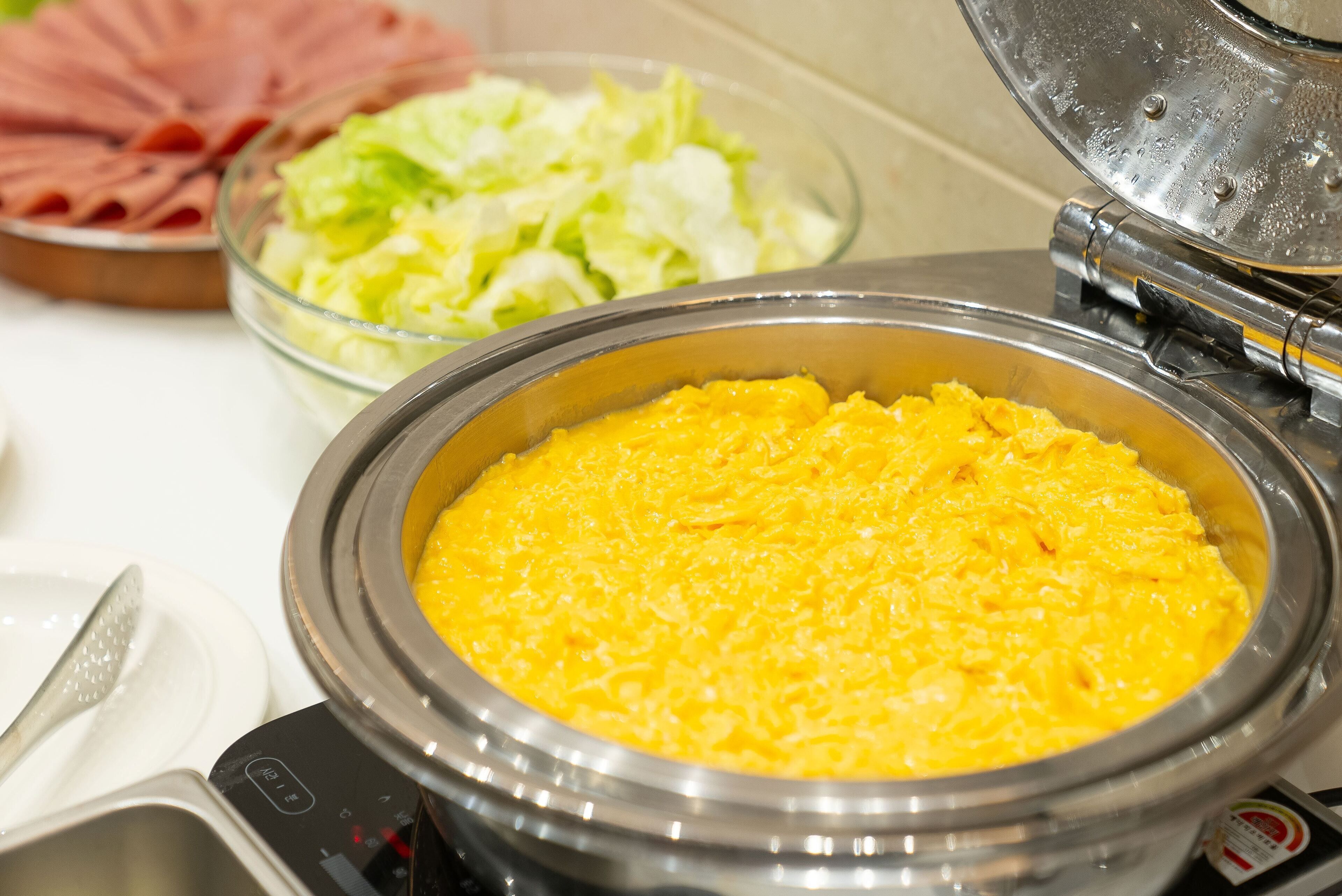 A buffet with a variety of food items including a bowl of scrambled eggs, a salad, and sliced meats.