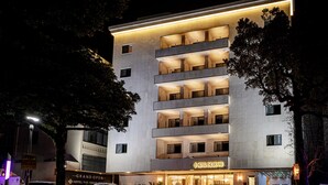 A multi-story hotel with a modern design, featuring balconies on each floor, a well-lit entrance, and a visible sign for the hotel. - Hotel The Grang Seogwipo (Seogwipo)