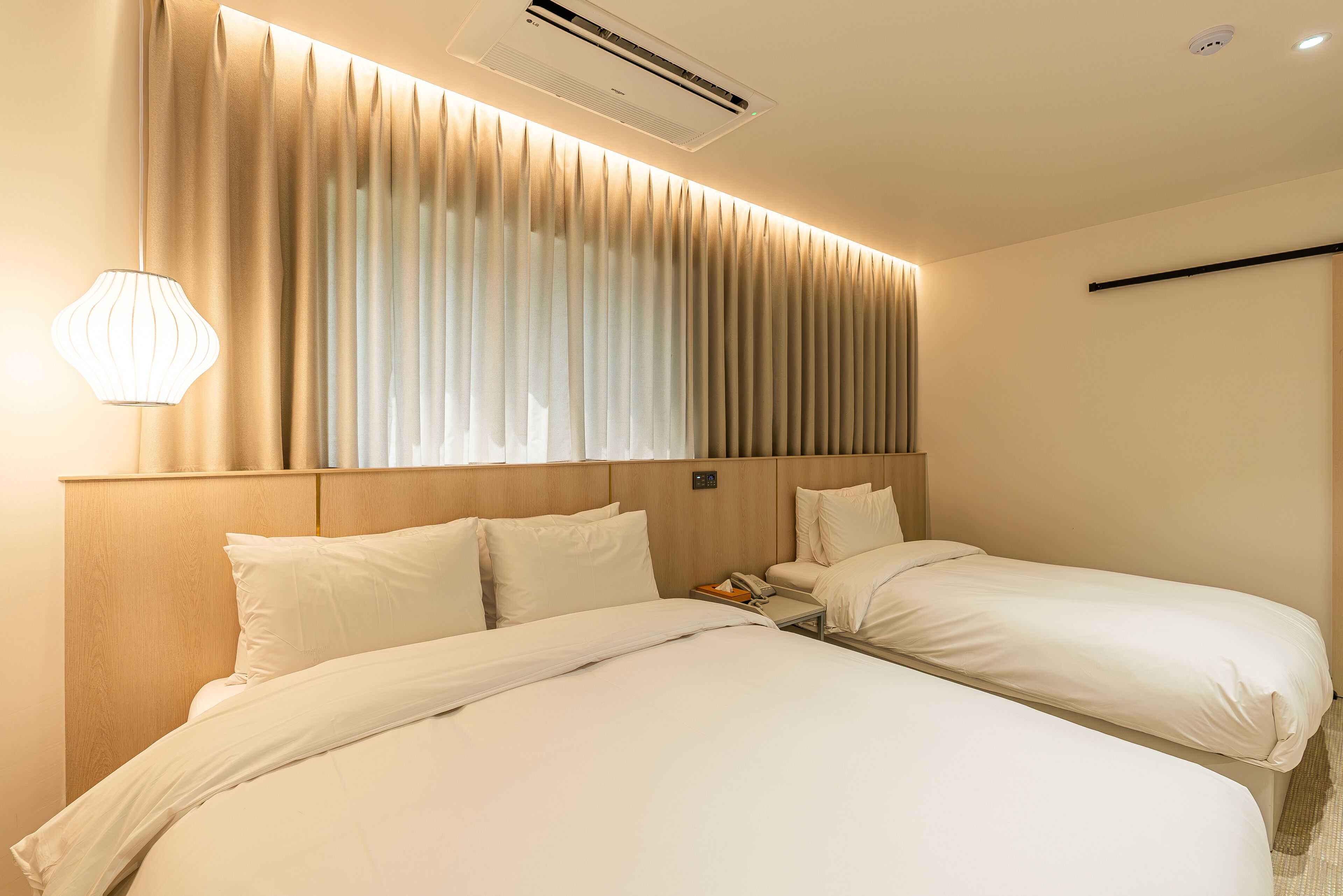 Ein Hotelzimmer mit zwei Betten, einem Nachttisch mit Lampe und einem Fenster mit Vorhängen.