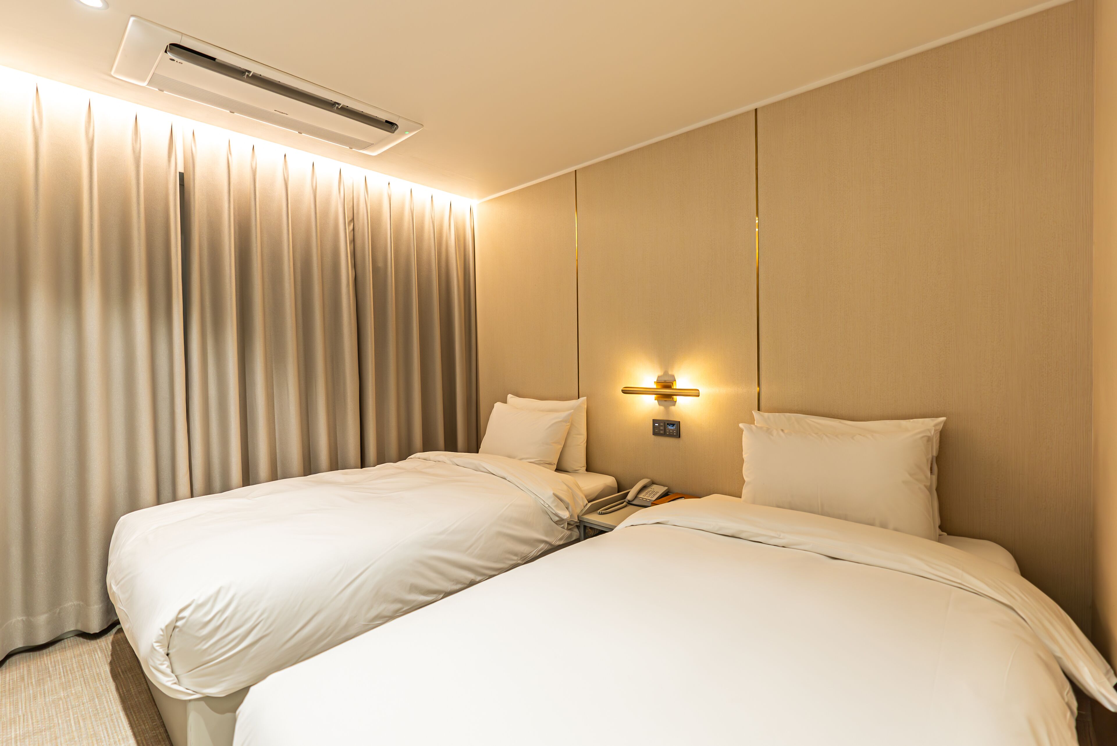 A hotel room with two beds, a wall-mounted phone, and an air conditioning unit.