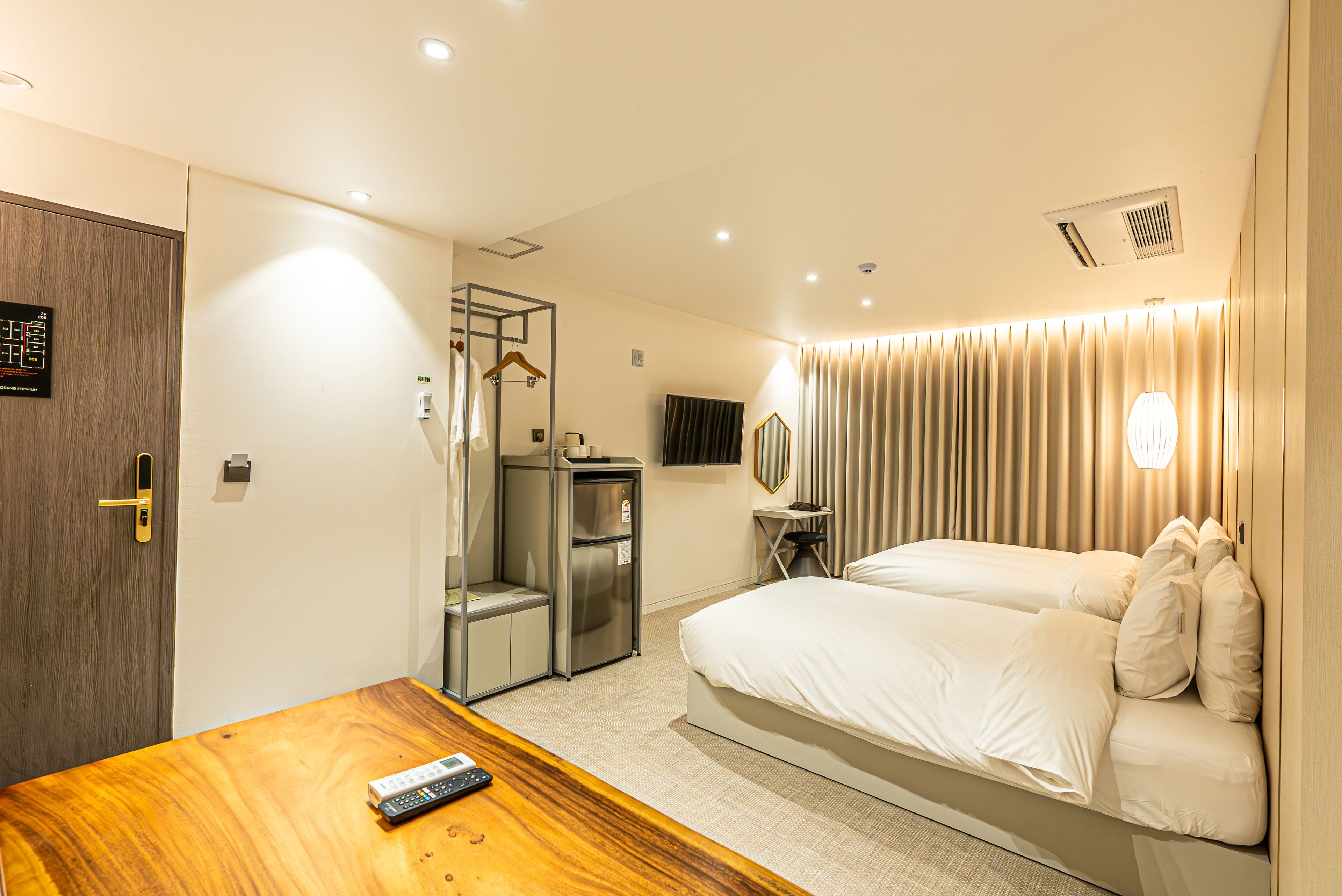 A hotel room with a bed, a wooden desk, a wardrobe, a mirror, a coat rack, and a minibar.