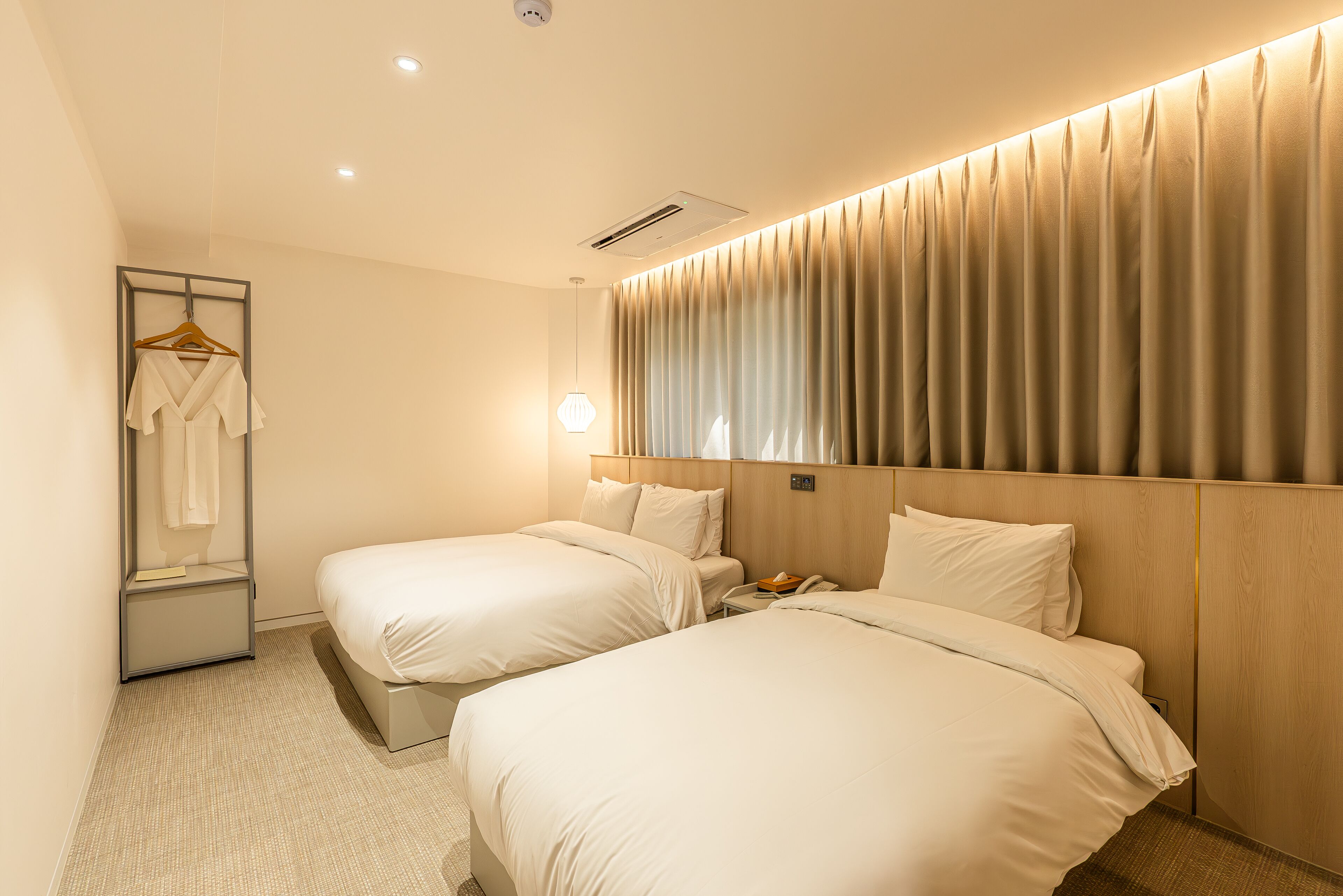 Habitación de hotel con dos camas, una mesita de noche con lámpara, bata colgada y un espejo.