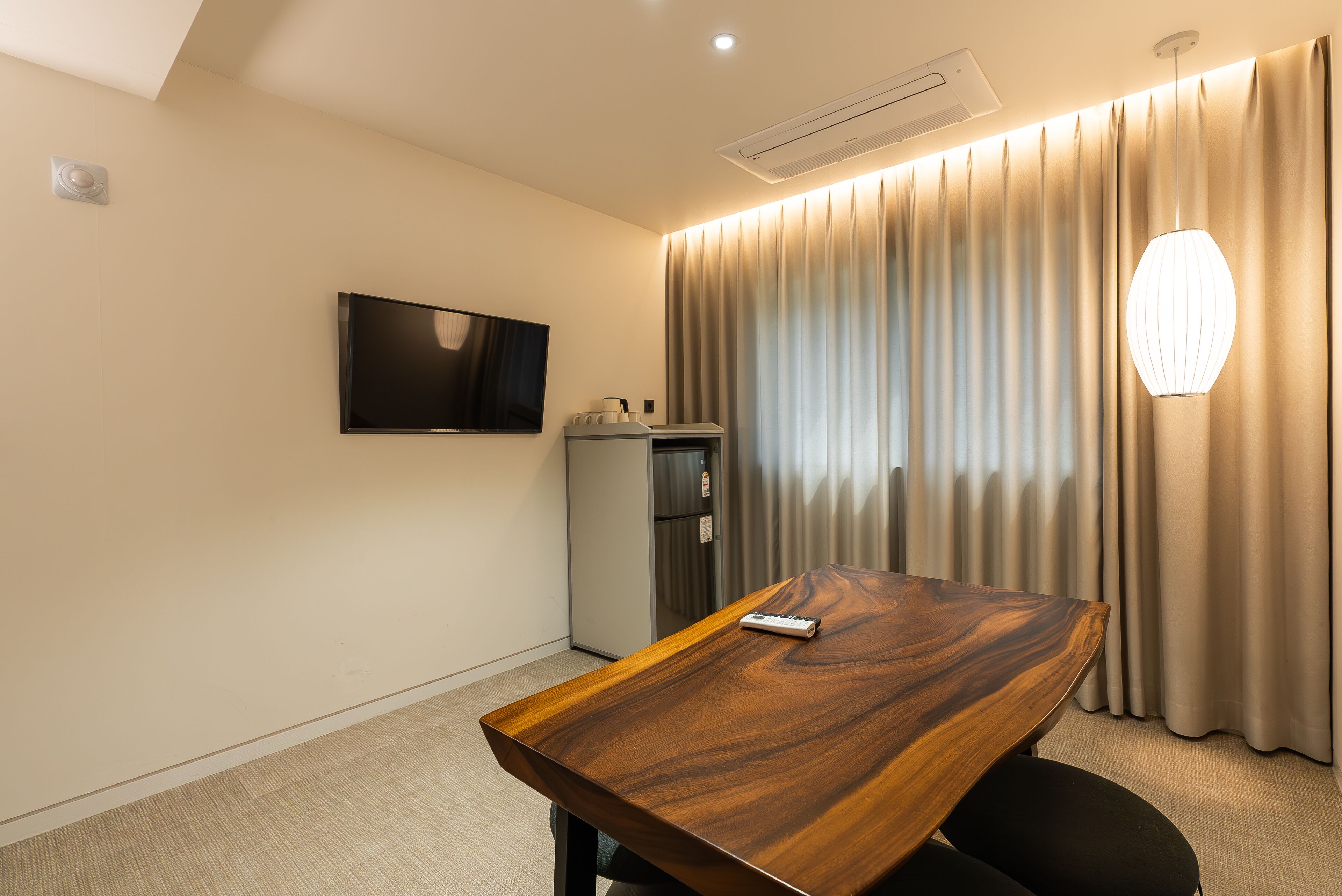Une chambre d’hôtel avec une table en bois, un téléviseur à écran plat, un minibar et une grande fenêtre avec des rideaux.