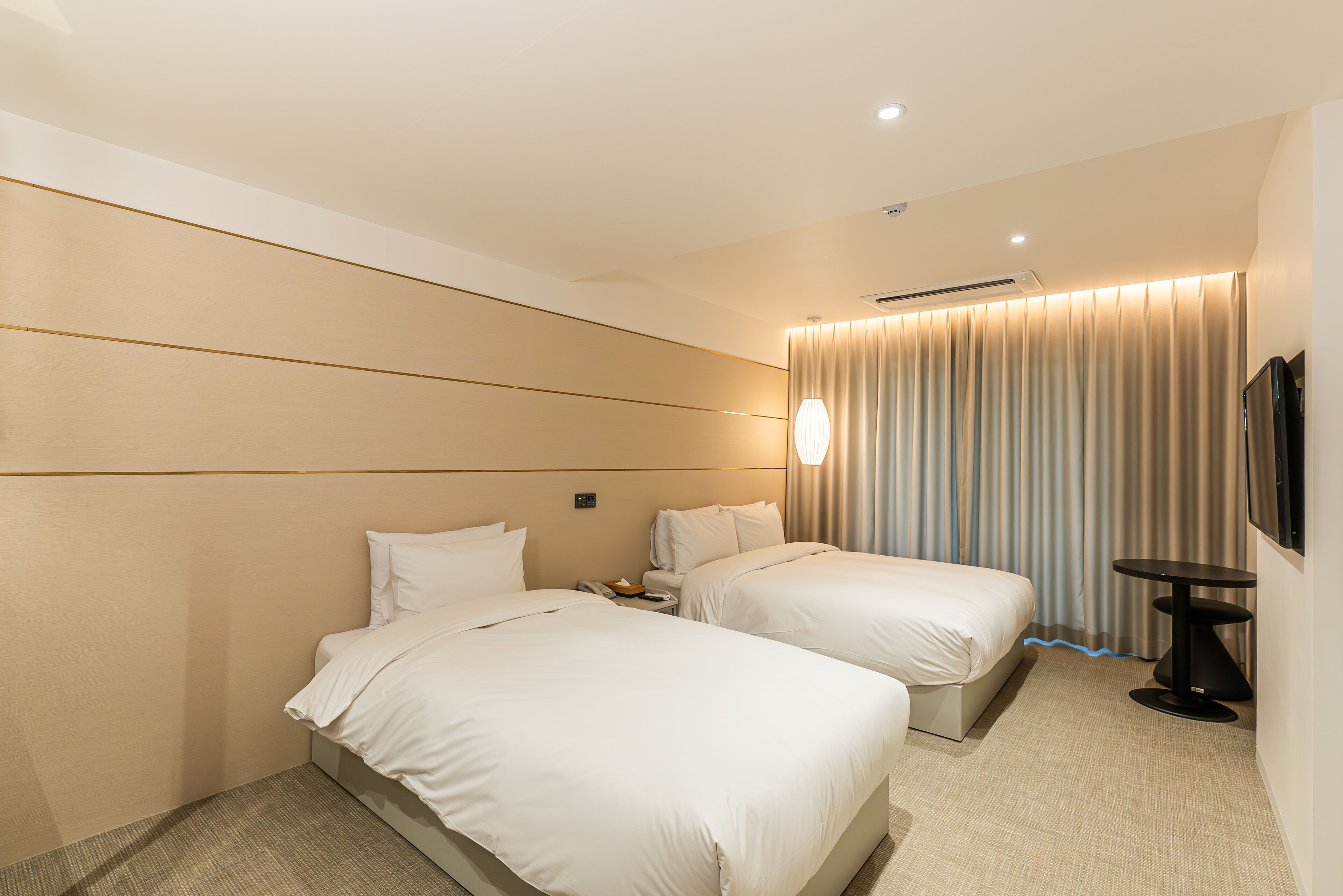 A hotel room with two beds, a flat-screen TV, a small table, and a curtain.