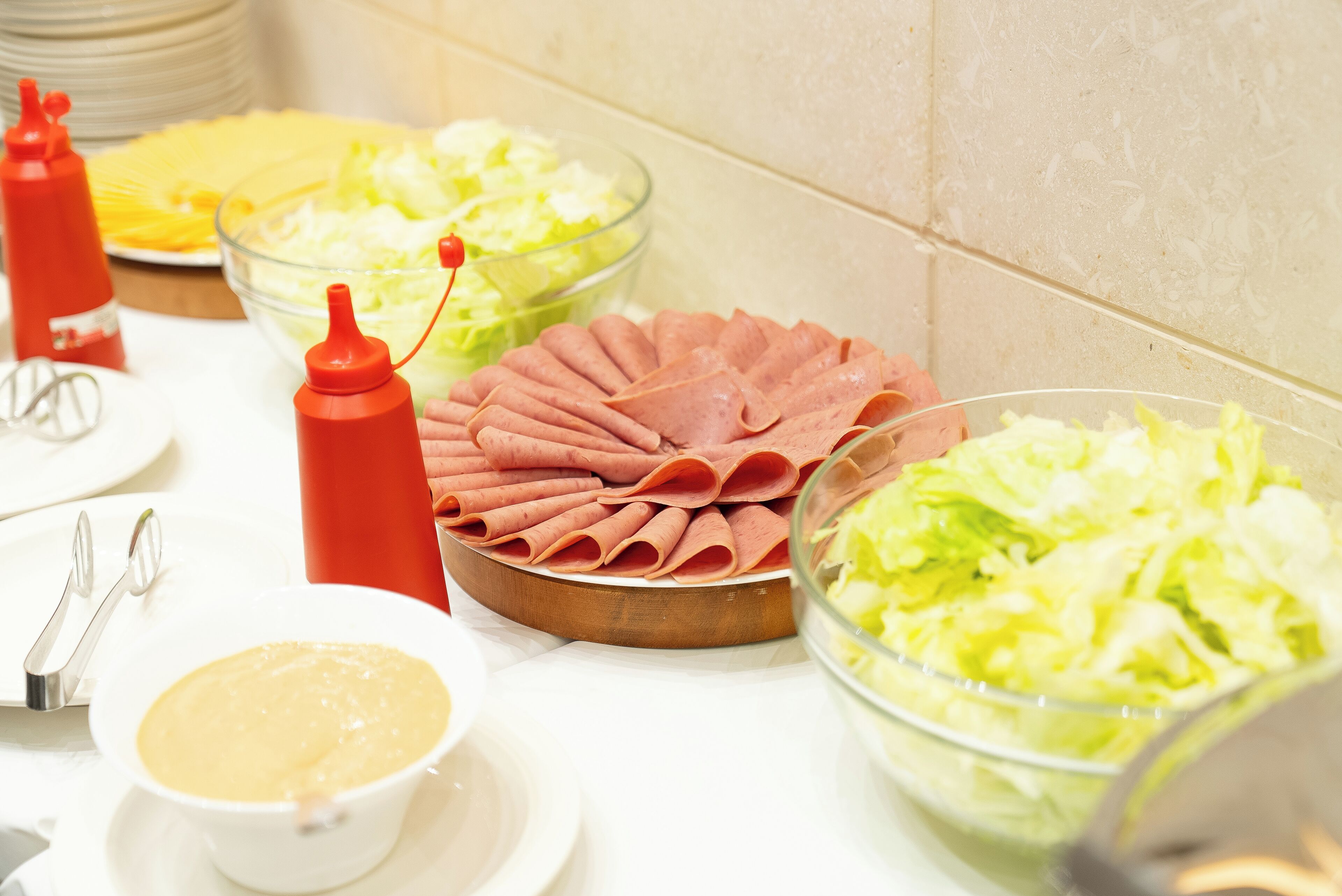 A buffet table with various food items including sliced ham, coleslaw, and a bowl of soup.