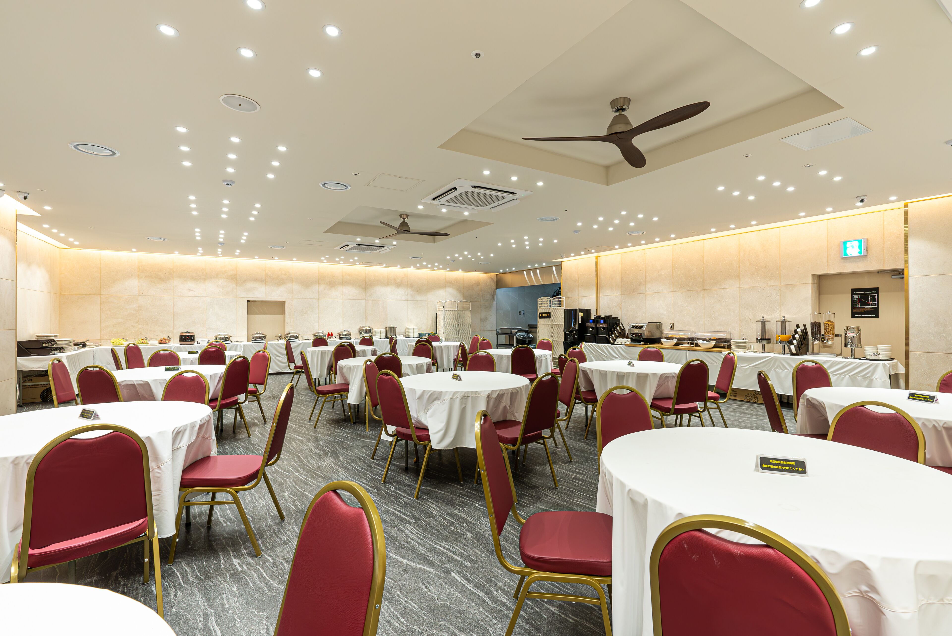 Un salón de banquetes con mesas redondas y sillas rojas, equipado con ventiladores de techo e iluminación empotrada.
