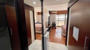 A hotel room with a bed, a desk, a chair, a TV, and a balcony with a view. - Três de Julho Flats - Paulista (São Paulo)