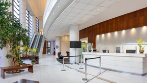 A modern hotel lobby with a reception desk, seating area, and an escalator. - Três de Julho Flats - Paulista (São Paulo)
