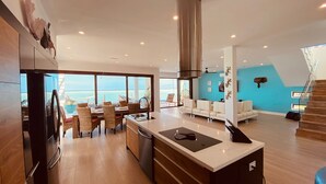 A modern kitchen with a large island, dining area with wicker chairs, and a view of the ocean.